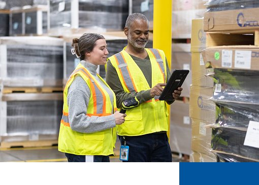 Two employees in warehouse using logistics software.